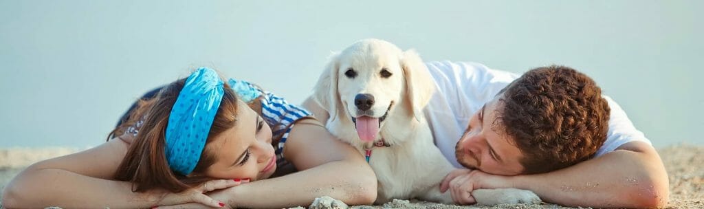 A woman and man lying down on sand with a dog in between them